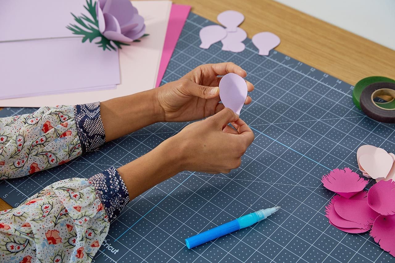 Persona armando una flor de papel con materiales Cricut sobre una tabla de corte